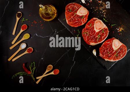 Raw beef shank bone in and spices for preparing ossobuco dish on black background. Top view. Stock Photo