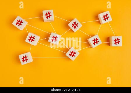Hashtag symbols on wooden cubes connected to each other with lines on yellow background. Hashtag connection, search or trending topic in social media Stock Photo