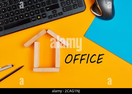 Home office or working from home concept. Overhead workspace with home icon made with wooden blocks and handwritten office word on yellow background. Stock Photo