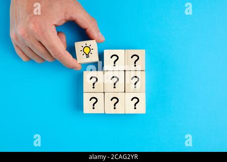 Concept of  problem solving, creativity, idea or innovation. Male hand places a wooden cube with hand drawn light bulb next to the cubes with question Stock Photo