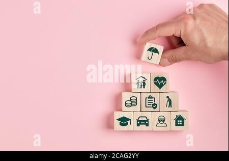 Insurance service concept. Wooden blocks with various types of insurance icons with a human hand placing one cube at the top. Stock Photo