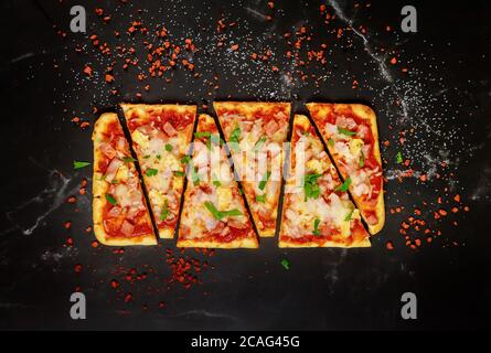 Sliced Hawaiian pizza with ham and pineapple on black stone background, top view. Stock Photo