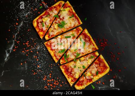 Cut into slices hawaiian pizza with ham, cheese and pineapple on a dark background. Top view. Stock Photo
