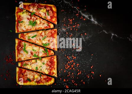 Slices of homemade hawaiian pizza with ham and pineapple topping on black background. Stock Photo