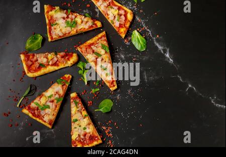 Cut into slices hawaiian pizza with ham, cheese and pineapple on a dark background. Top view. Stock Photo