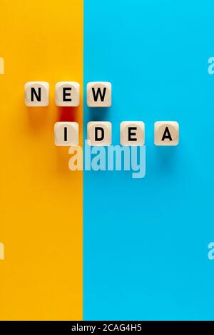 The word new idea written on wooden cubes on yellow and blue background. Finding and implementing new ideas concept. Stock Photo