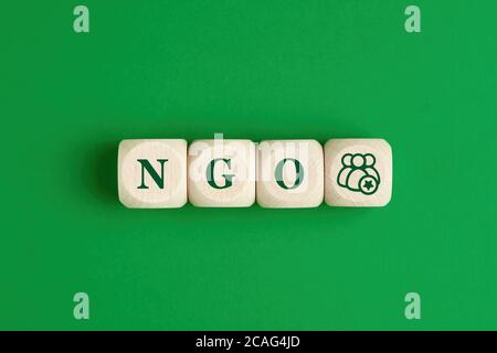 The abbreviation word NGO nongovernmental organization written on wooden cubes with group of people icon on green background Stock Photo