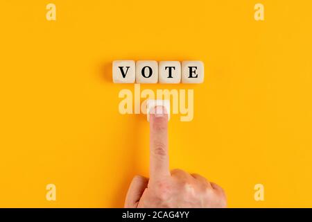 The word vote written on wooden cubes with a male hand pushing the voting button. Online voting concept in politics or business meetings. Stock Photo