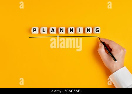 Male hand underlines the word planning written on wooden blocks on yellow background. Concept of business planning. Stock Photo