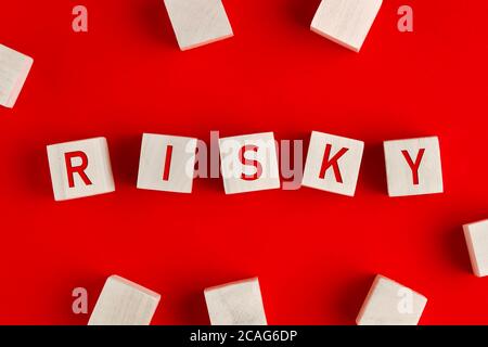 The word risky written on wooden blocks on red background. Concept of risk management or assessment and decision making in an uncertain business envir Stock Photo