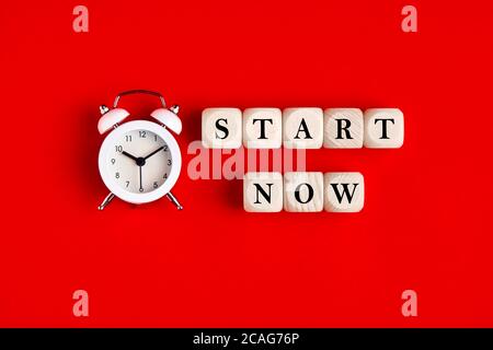 The word start now is written on wooden blocks with an alarm clock. Timing, motivation, strategy and action concept. Stock Photo