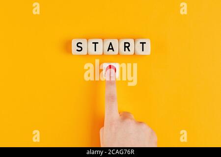 The word start on wooden cubes with a male hand pressing the start button. To make a new start in life, business, education or career concept. Stock Photo