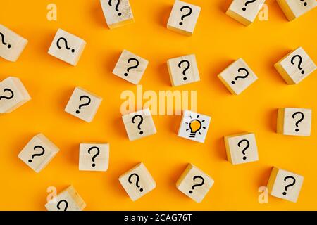 Concept of to find a creative idea or problem solving. Question mark and light bulb icons on wooden cubes on yellow background. Stock Photo