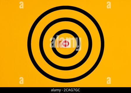 Target with the word win written on a wooden block as the bulls eye on yellow background. Concept of focusing on a win in competition. Stock Photo
