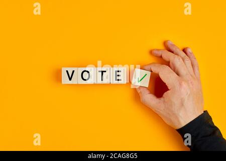 Male hand placing wooden cube with checkmark yes symbol next to the cubes with the word vote. Concept of voting yes or positive vote. Stock Photo