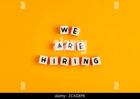 We are hiring text on wooden blocks against yellow background. Concept of human resources recruitment, employment or hire for a job. Stock Photo