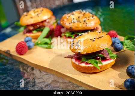 Set of tasty fresh homemade burgers with bacon, basil, blueberry, tomatos, raspberry on the wooden plate Stock Photo