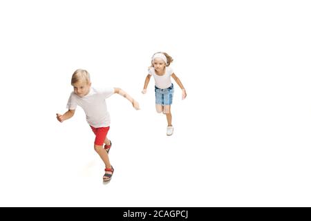Friendship. Happy kids, little emotional caucasian boy and girl jumping and running isolated on white background. Look happy, cheerful, sincere. Copyspace for ad. Childhood, education, happiness concept. Stock Photo