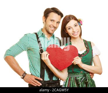 Happy couple in traditional Bavarian clothes holding a big red heart Stock Photo