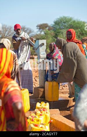 13.11.2019, Gabradahidan, Somali Region, Ethiopia - Women filling yellow water canisters at a water pump. A man pumps water from a cistern with the he Stock Photo