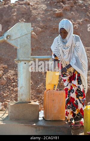 13.11.2019, Gabradahidan, Somali Region, Ethiopia - Woman fills a yellow water canister at a water pump connected to a cistern. Hydraulic engineering Stock Photo