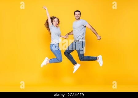 Excited lovely interracial couple holding hands smiling and jumping with joy isolated in yellow studio background Stock Photo