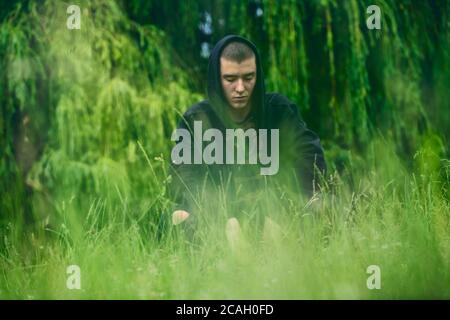 Portrait of a sad, crouching man in a black hoodie Stock Photo