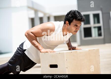 Handsome Indian sports man doing push up exercise outdoors on building rooftop, home workout concept Stock Photo