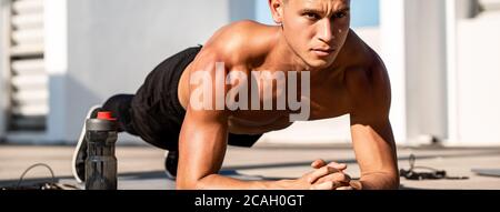 Banner image of handsome muscular sports man doing plank exercise outdoors on rooftop Stock Photo