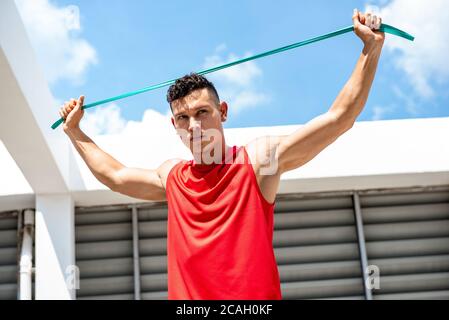 Handsome athletic man stretching with resistance band outdoors on building rooftop, home exercise concept Stock Photo