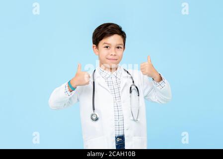 Smiling handsome little kid doctor giving double thumbs up isolated on light blue studio background Stock Photo