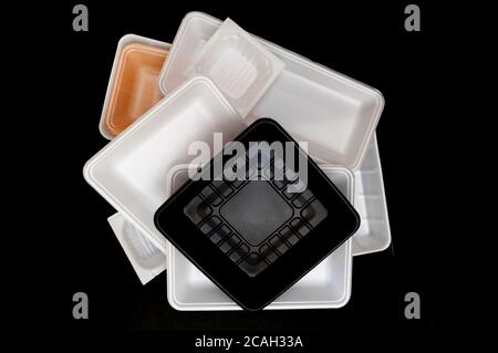 Foam food container tray (Styrofoam tray). Various Styrofoam trays of colors: orange, white and black isolated on black background. Horizontal shot. Stock Photo