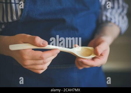 A chef in a blue apron holds a wooden kitchen utensil - an elegant handmade spoon that will be used in the work. Stock Photo
