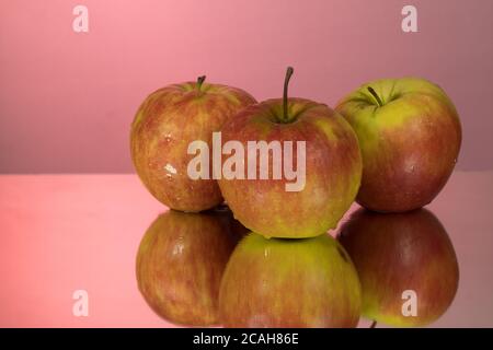 Three red apples on mirroring table on mirror red background with reflection isolated close up Stock Photo
