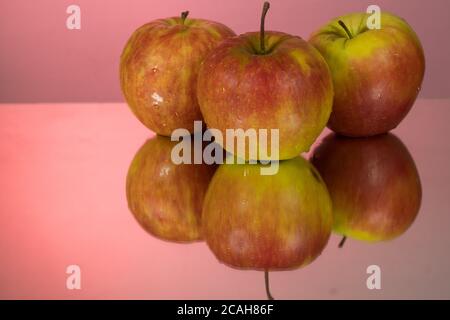 Three red apples on mirroring table on mirror red background with reflection isolated close up Stock Photo