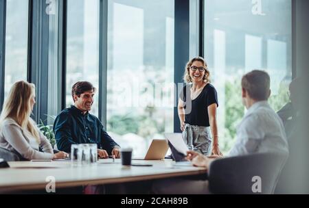 Office colleagues having casual discussion during meeting in conference room. Group of men and women sitting in conference room and smiling. Stock Photo