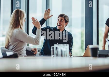 Happy and successful business colleagues giving high five in office. Coworkers sitting in conference room celebrating success. Stock Photo