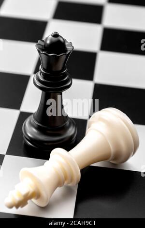 Checkmate, gender issues and fall of powerful leader concept with fallen white king and standing black queen on chess board Stock Photo