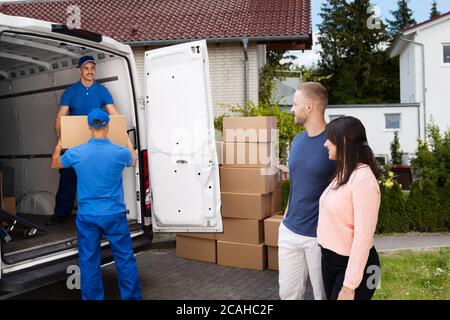 Happy Family Couple Watching Movers Unload Boxes From Truck Stock Photo