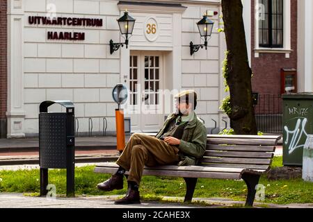 Haarlem, Netherlands 05/16/2010:  A young well dressed man wearing old style clothing is sitting crosslegged on a bench in front of a funeral home in Stock Photo