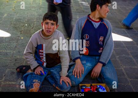 Damascus, Syria 03/28/2010: Teenager boy is sitting on his knees on cobblestone street floor of the Al Hamidiyah Souq (covered market) trying to sell Stock Photo