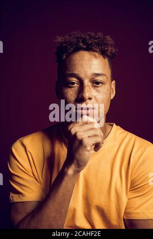 Young adult mulatto holding hand near face, looking at camera Stock Photo