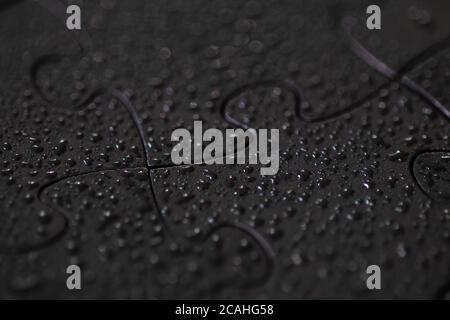 Macro view of black jigsaw puzzle pieces with water droplets and selective focus Stock Photo