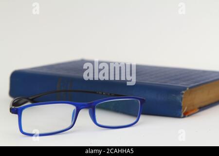 Hardcover beige book and reading glasses on white slate board. Stock Photo