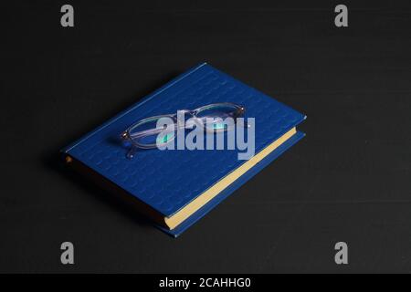 Hardcover beige book and reading glasses on black slate board. Stock Photo