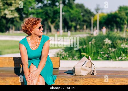 Mature woman sitting on the bench in the park in summertime Stock Photo