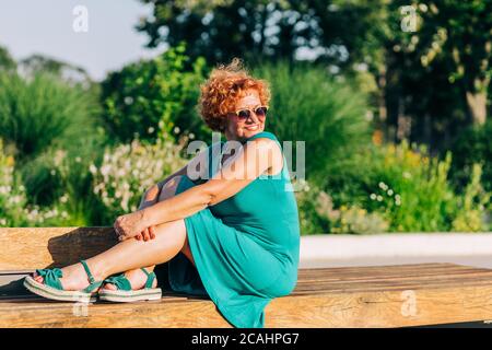 Mature woman sitting on the bench in the park in summertime Stock Photo