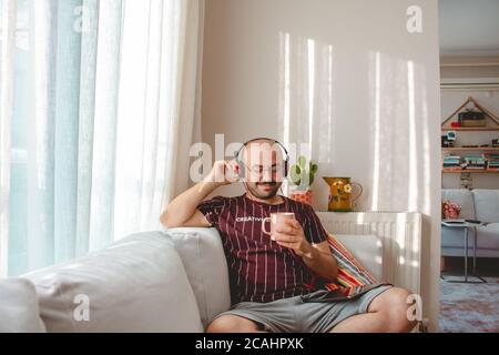 young people having a good time at home. listening to music, drinking coffee and tea. Resting teenager running with tablet and leptop in hands. Stock Photo