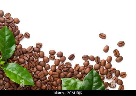 Spilled coffee beans with green leaves isolated on white background. Roasted arabica. Copy space. Top view Stock Photo