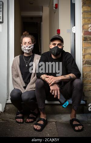 Two housemates wearing face masks sitting on the doorstep of their home during the COVID-19 lockdown, Stockwell, London Stock Photo